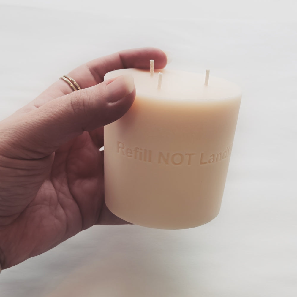 Hand holding a refill wax candle with 'Refill NOT Landfill' text on a light background by The Pure Light Company
