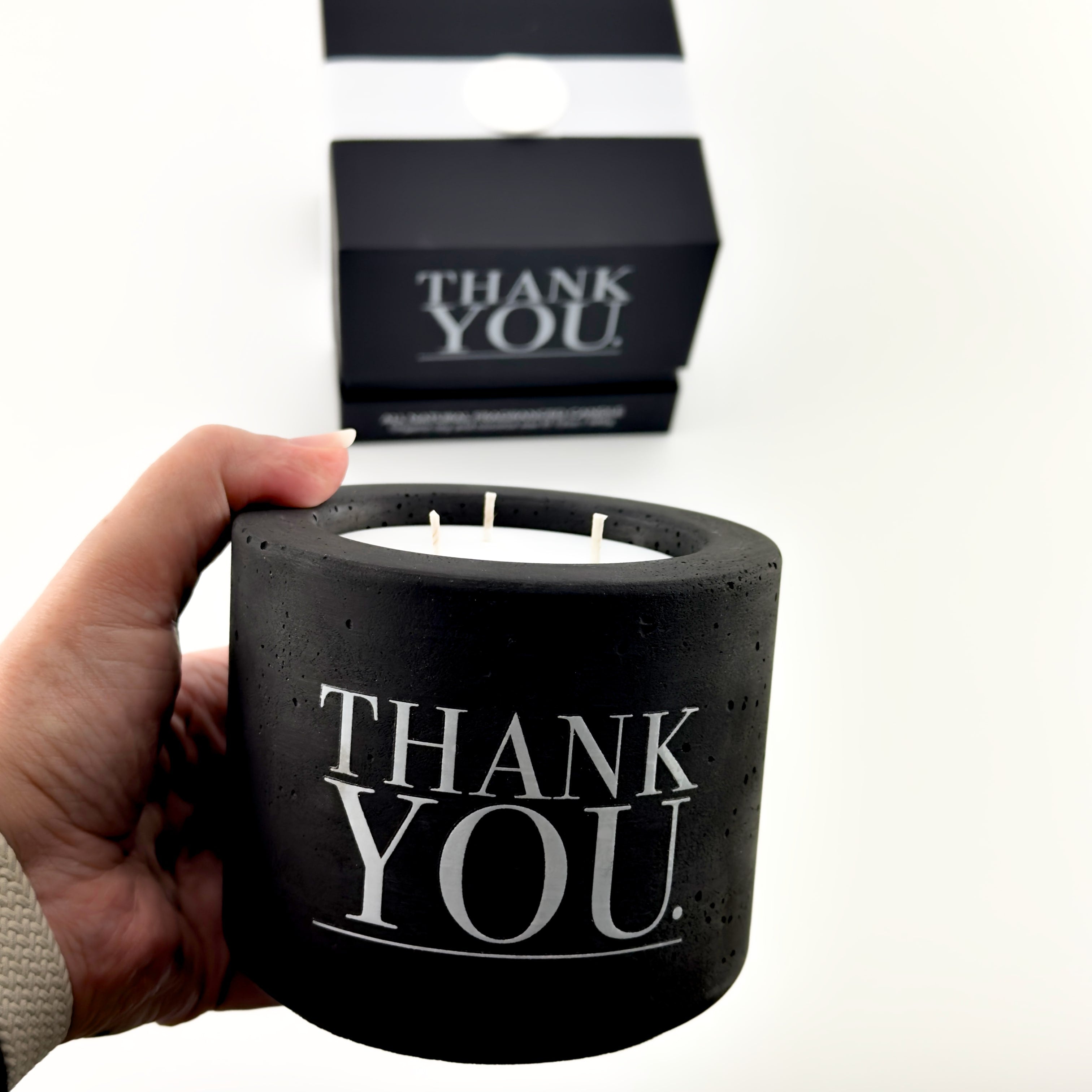 Black candle holder with 'THANK YOU' text held by a hand, with matching cards in the background.