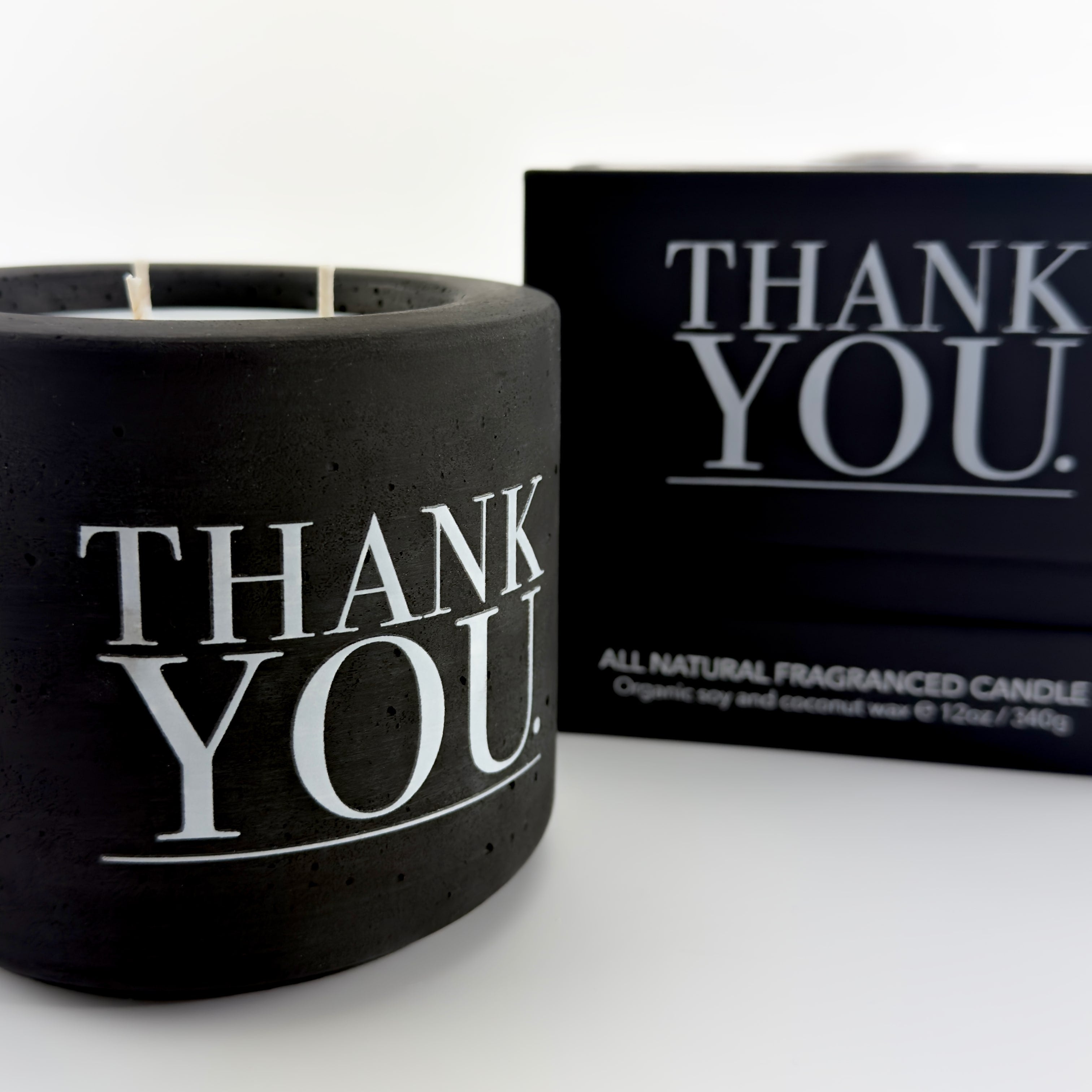 Black candle with 'THANK YOU' text and packaging on a white background by The Pure Light Company.