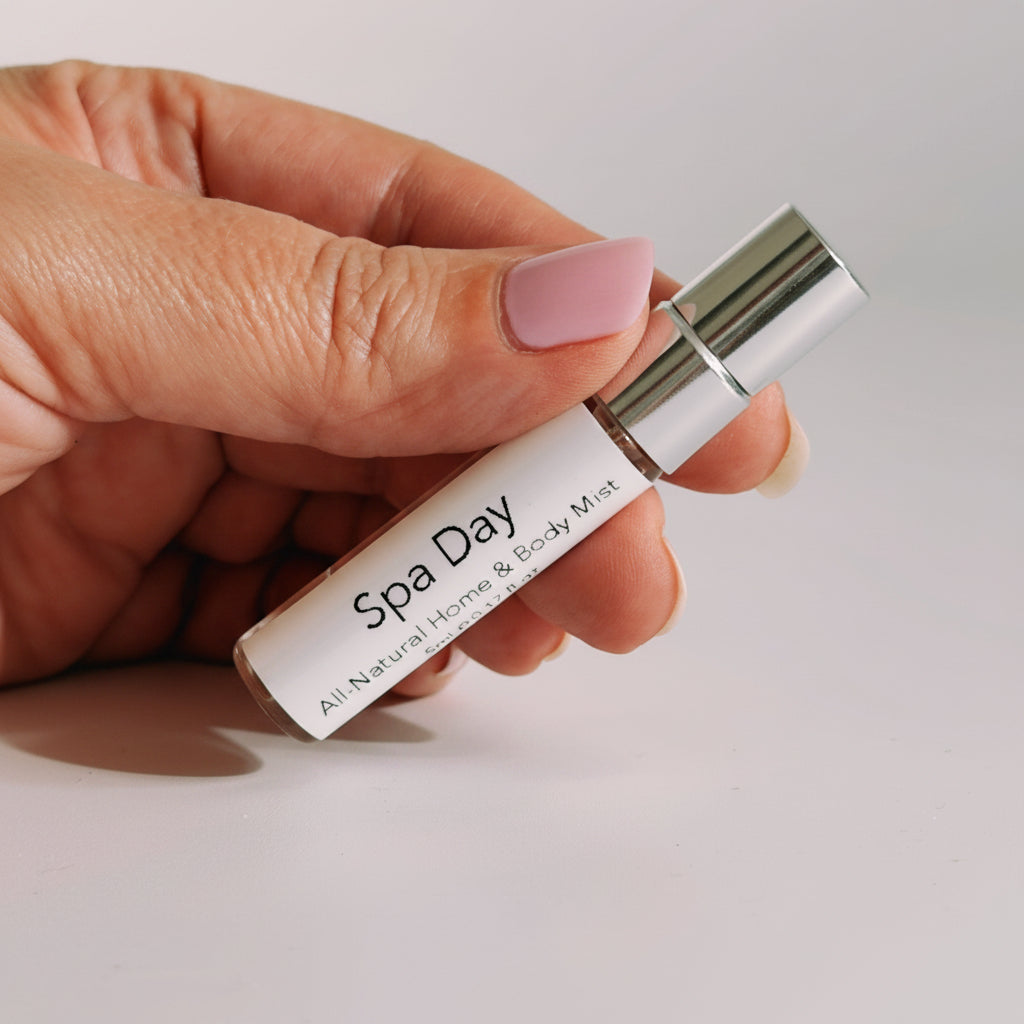 A hand holding a small white roll-on bottle labeled 'Spa Day' with a shiny silver cap against a plain light background by The Pure Light Company.